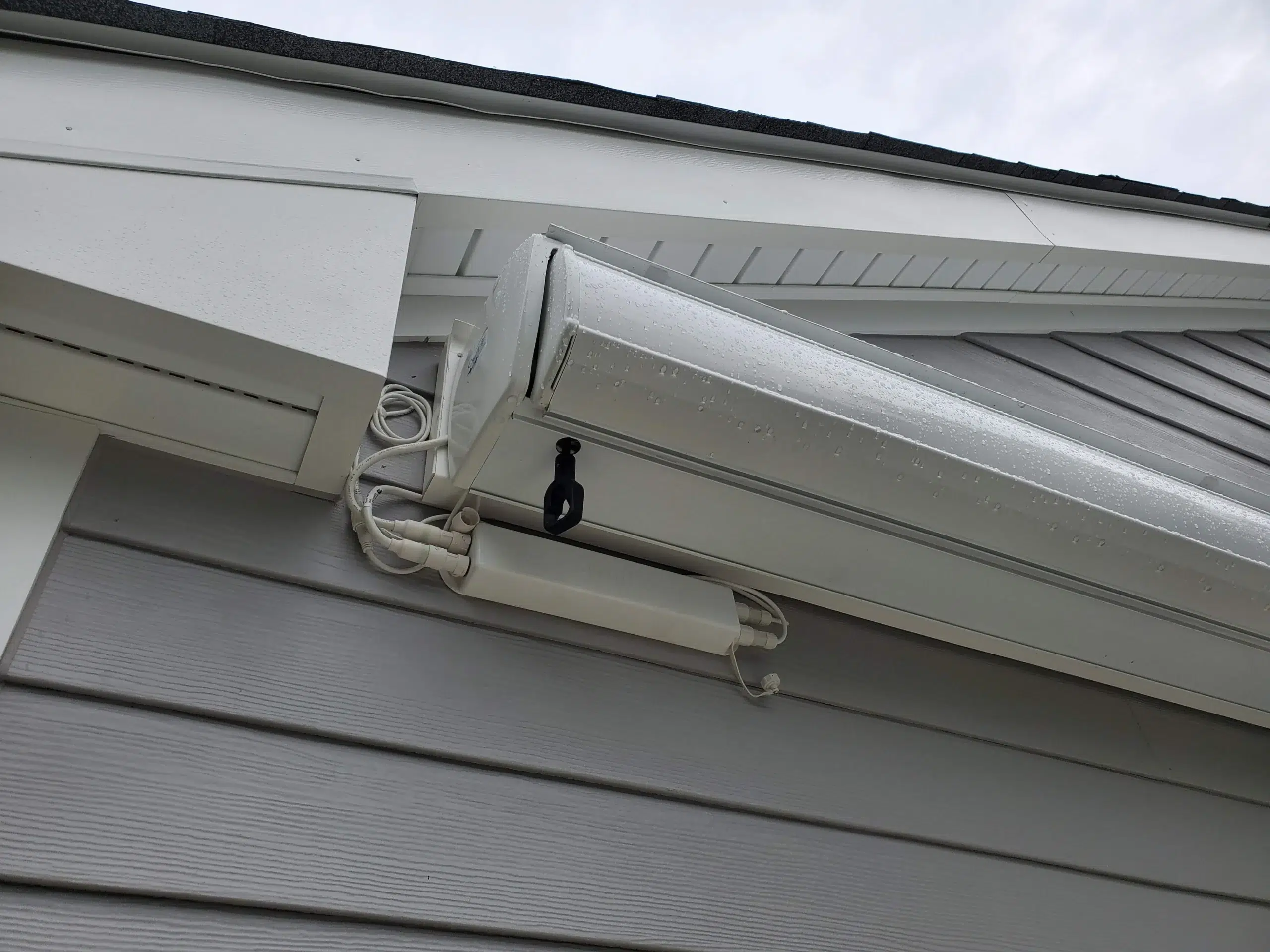 Close-up view of a retractable awning cassette and mounting hardware installed under the roofline of a gray home.