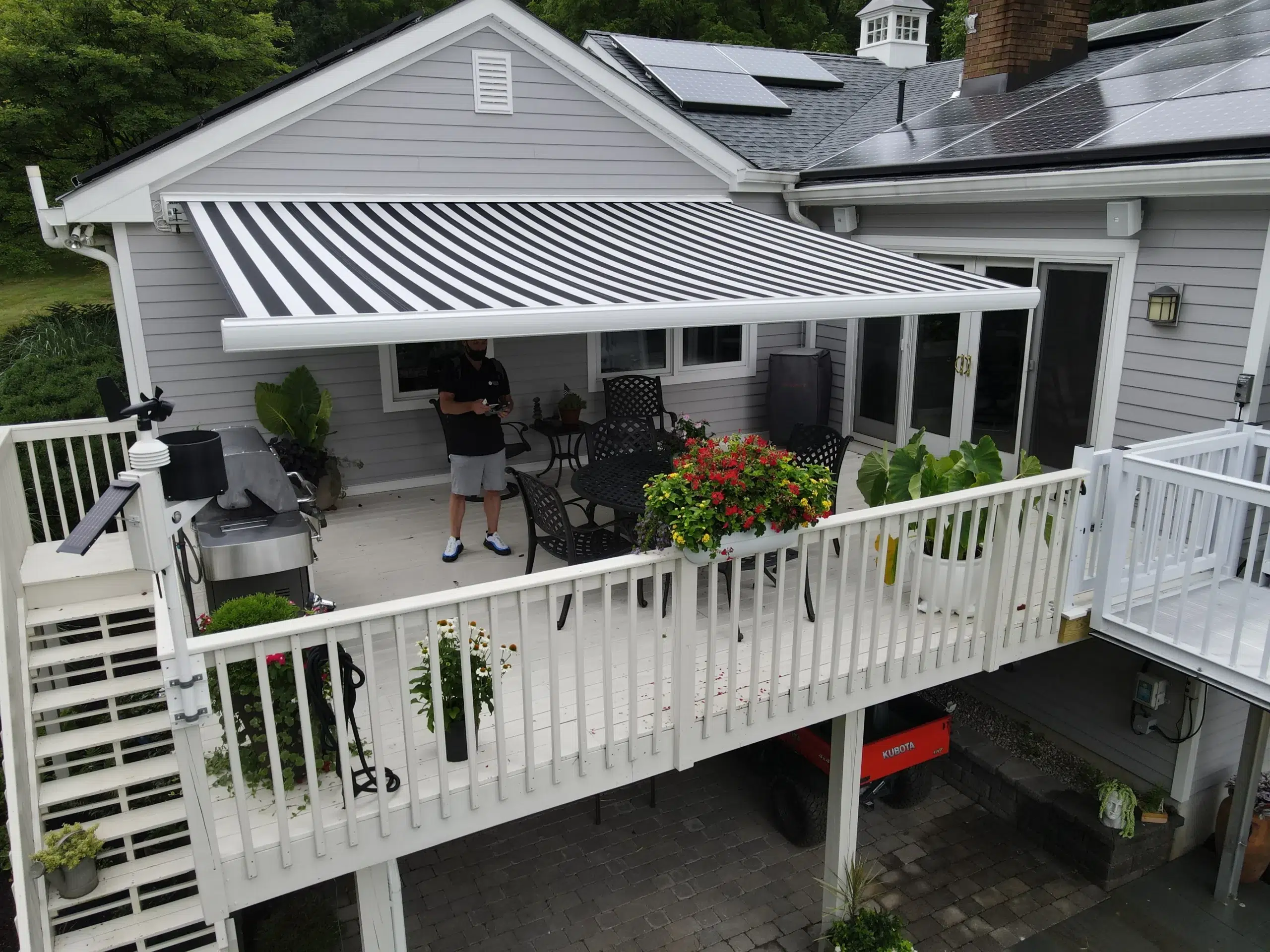 Black-and-white striped retractable awning extended over an elevated deck with outdoor seating, plants, and white railings.