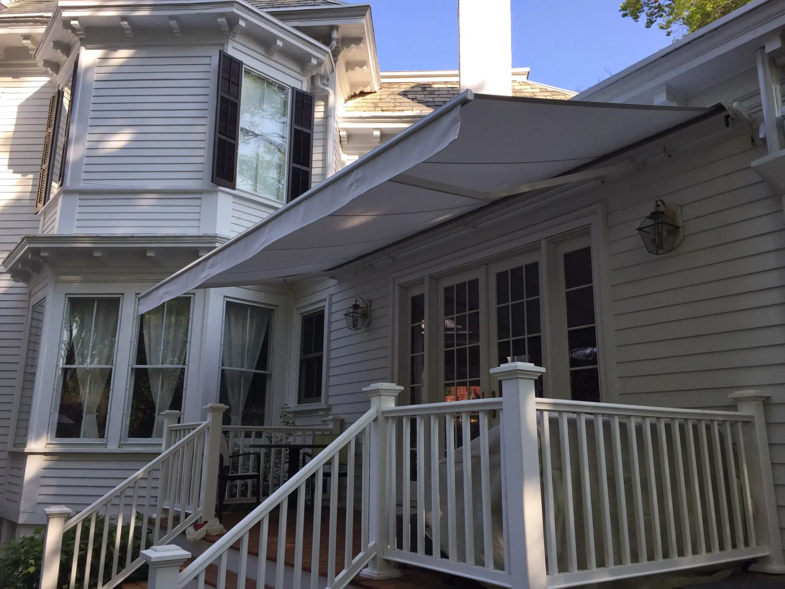 Retractable awning extended above a white porch deck with railings on a traditional-style home with double doors.