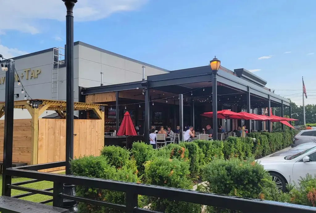 A lively outdoor dining area with red umbrellas, surrounded by lush greenery, showcasing a vibrant restaurant ambiance under a blue sky.