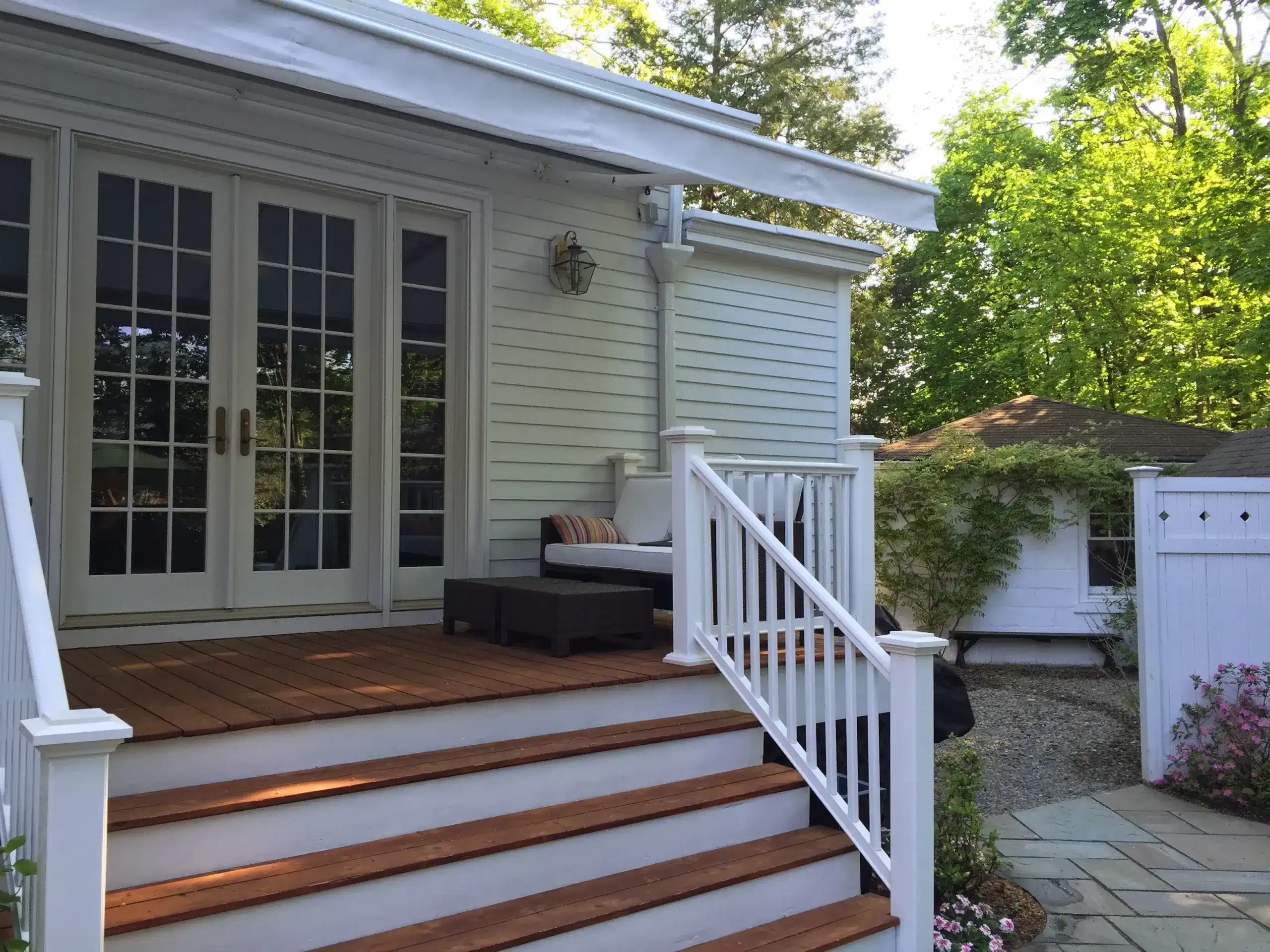 Retractable awning installed above a raised porch with wooden steps, white railings, and French doors leading into the home.